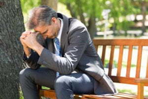 businessman with head in hands on park bench