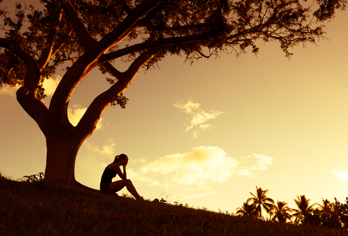 silhouette of woman sitting outside with head in hands