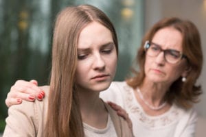 mom with hands on sad daughter's shoulder