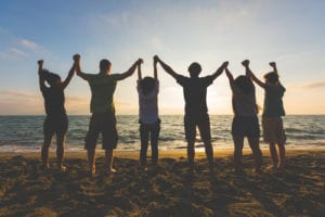 people holding hands and facing ocean