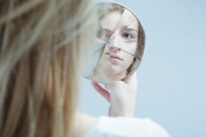 woman viewing self in cracked small mirror