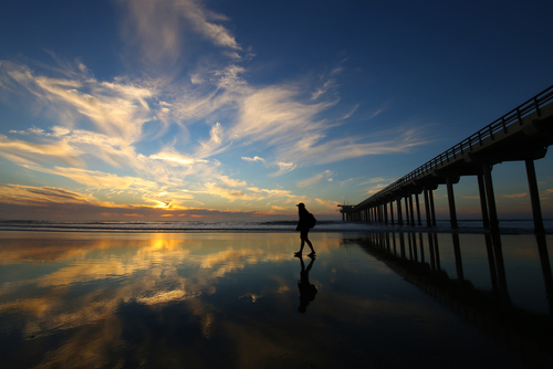 silhouette of person walking by pier
