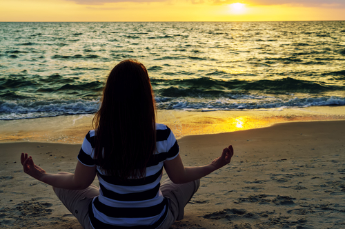 woman in clothes meditating on beach
