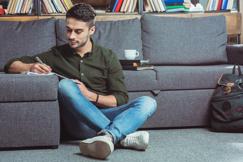 man seated on floor writing