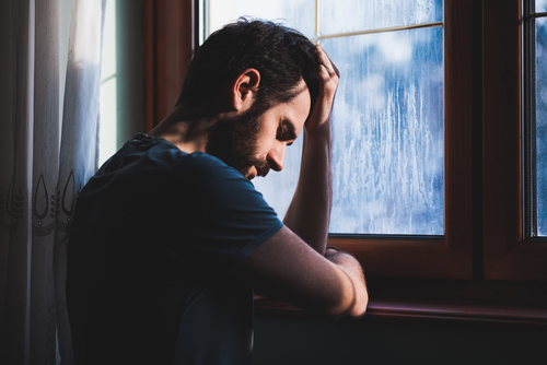 man with head in hands at window