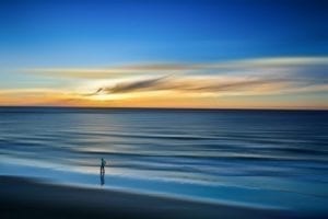 Man walking beach in Tel Aviv-Yafo with sunset reflecting over ocean