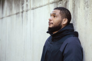 Portrait of a black man, in profile, with dramatic and worried expression. A street wall in the background. Workers, unemployment, students and black people concept.Copyspace